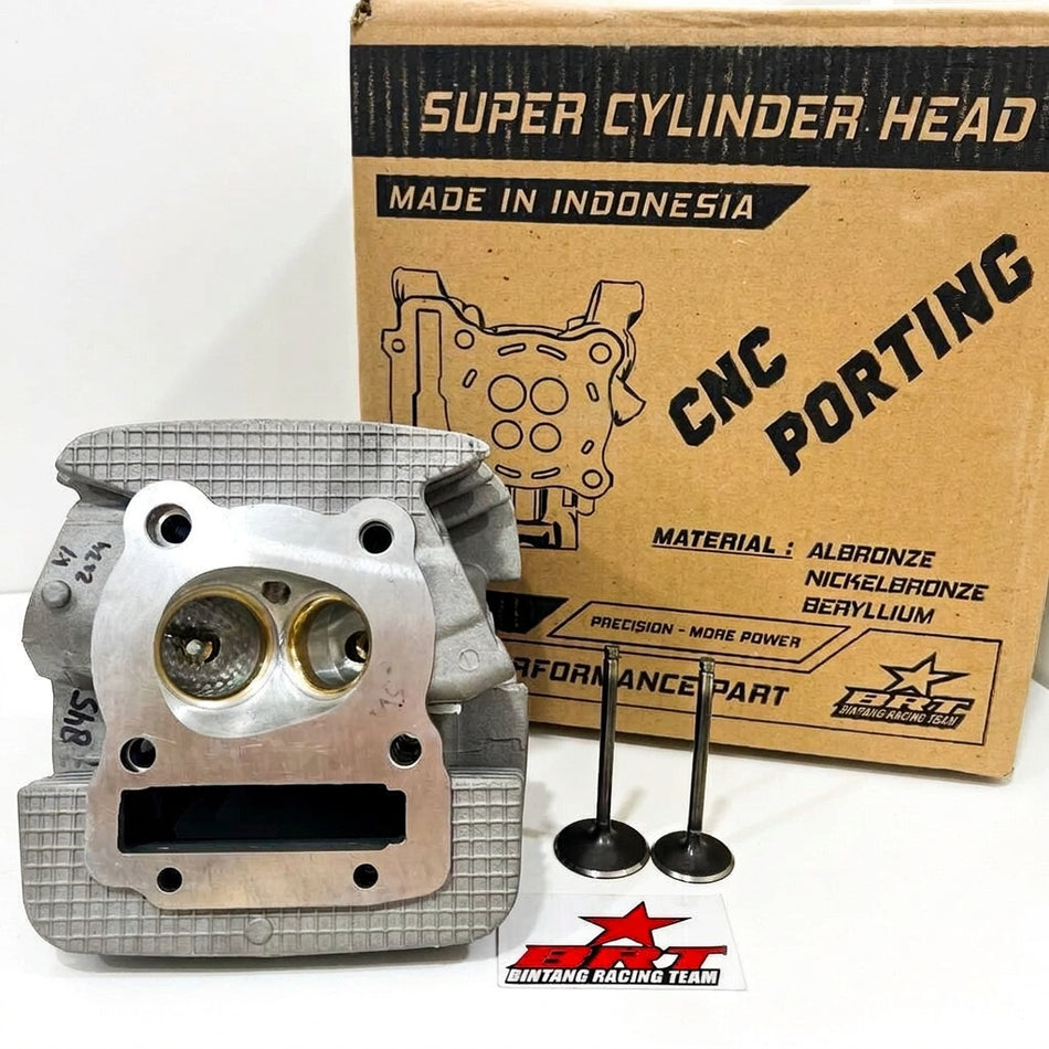 A silver aluminum motorcycle cylinder head shown in front of its brown cardboard packaging box, with two black valve stems and a small yellow paper insert on a white background.